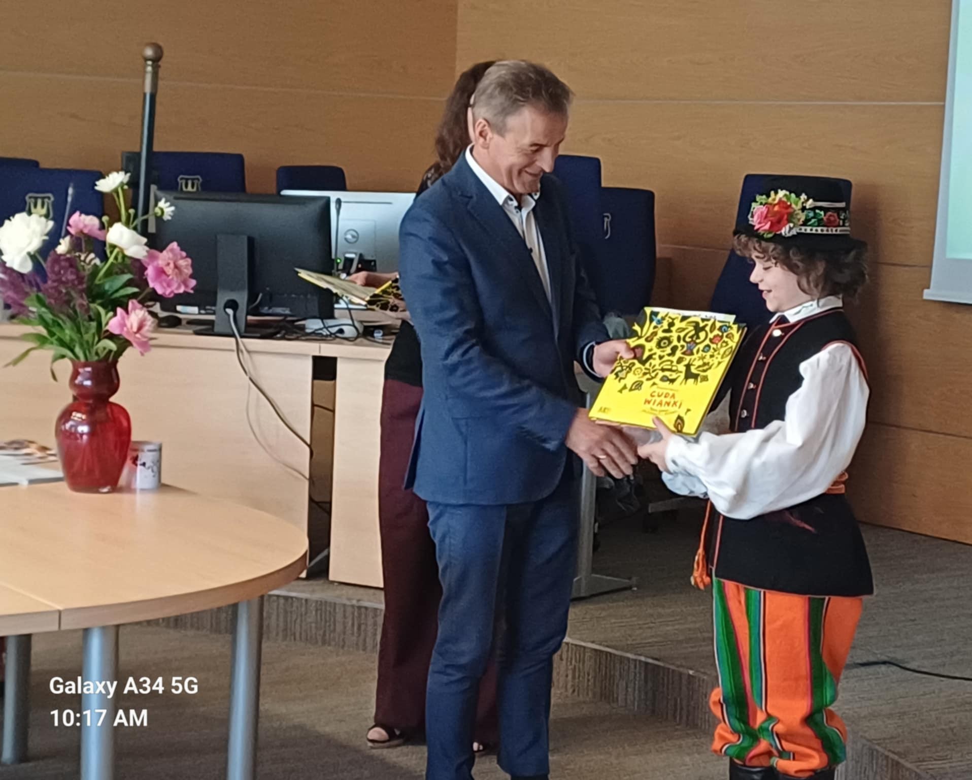 Pan Burmistrz Zenon Reszka podaje chłopcu w łowickim stroju książkę