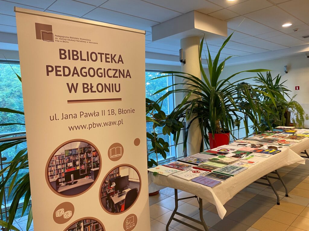 Baner biblioteki i książki - prace uczniów na stole. W tle rośliny doniczkowe.