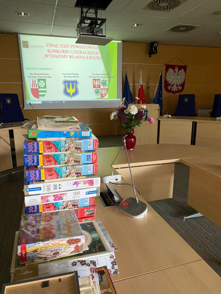 Nagrody konkursowe. W tle slajd informujący o wydarzeniu i sponsorach nagród.
